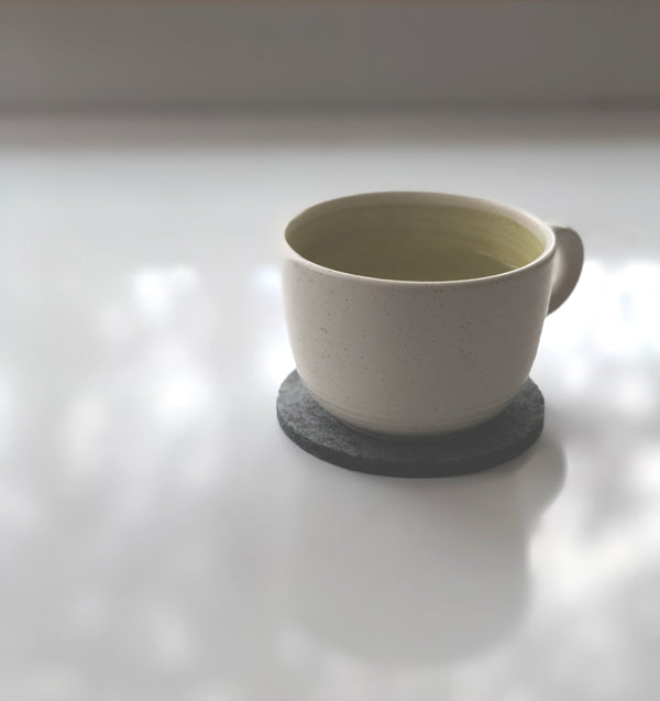 Peaceful scene of a cup of tea sitting on a grey wool felt coaster on a white counter